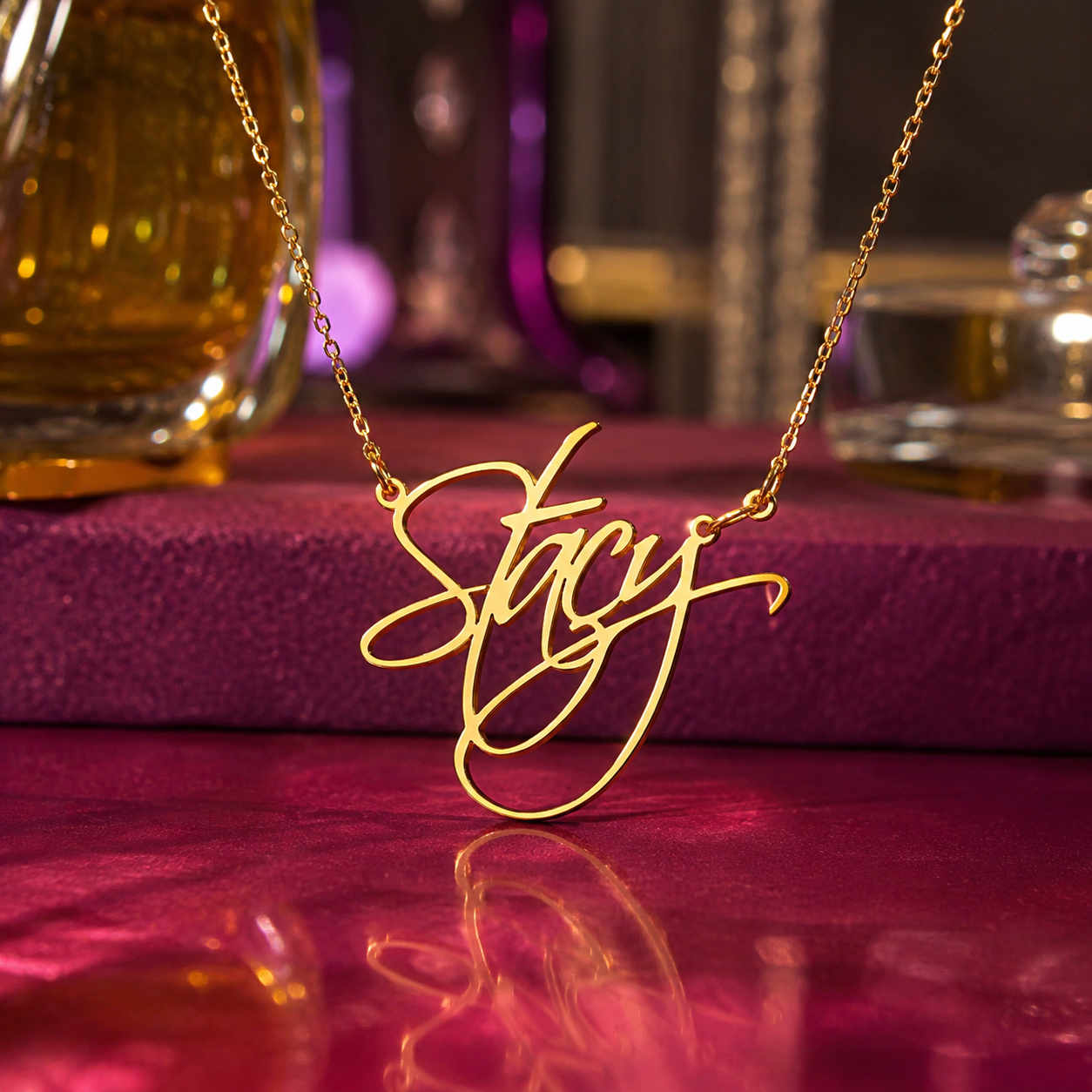 A gold nameplate necklace spelling 'Stacy' in elegant cursive script, hanging on a delicate gold chain against a dark, moody background with purple and gold tones.