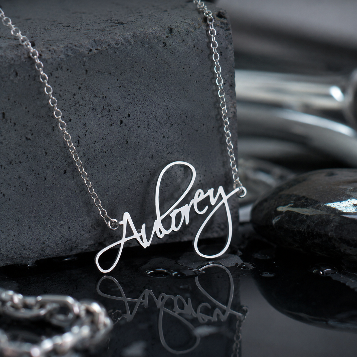 Personalised stainless steel Flame Script name necklace displayed on a dark reflective surface